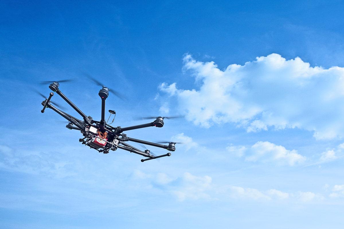 octocopter flies high with bright blue sky and clouds in the background.